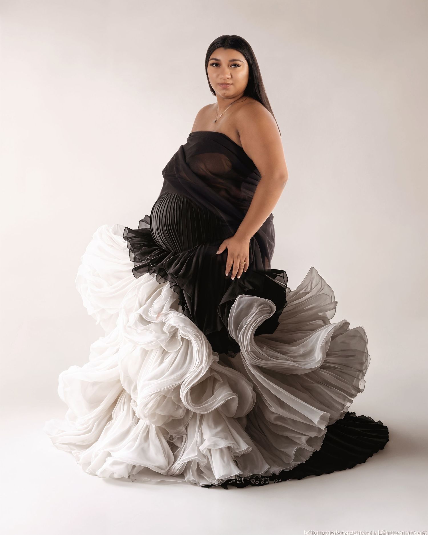 A dramatic black and white gown with flowing ruffles and ombre effect transitions from dark to light in a studio setting.