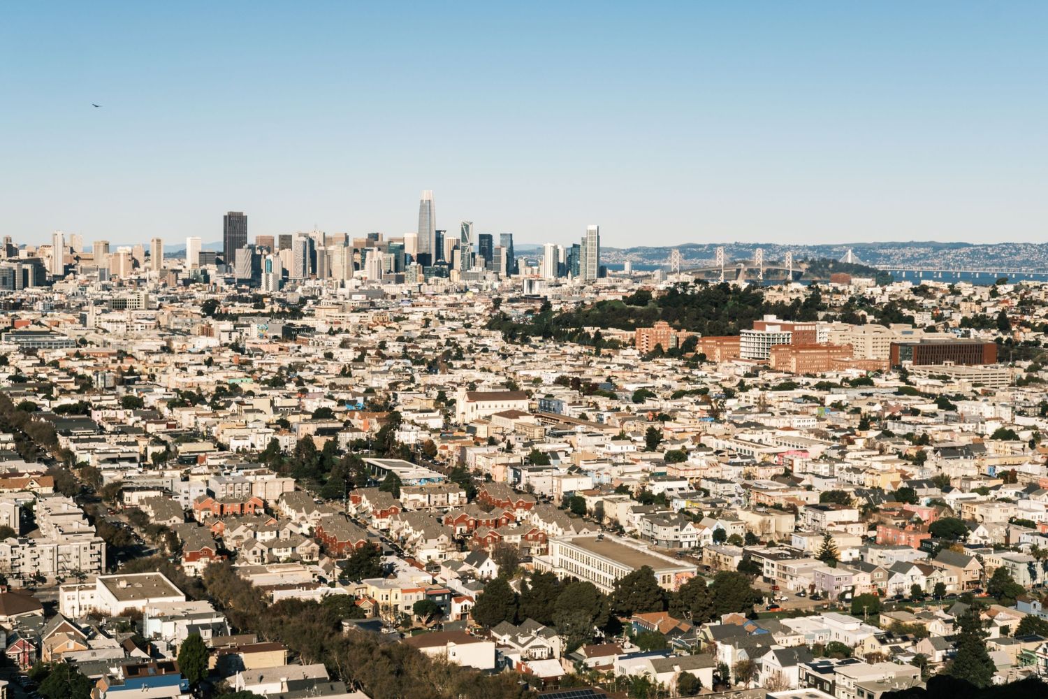Panoramic aerial view of San Francisco cityscape with iconic downtown buildings and residential neighborhoods stretching to horizon.