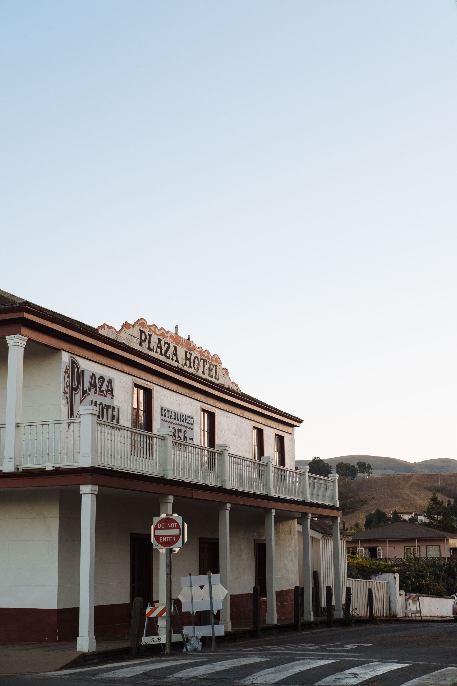 Historic Plaza Hotel building with white walls and balcony stands on corner street in small town at dusk.