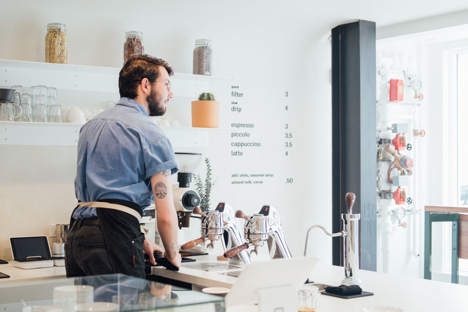 Barista working at a modern coffee counter with equipment and menu board.