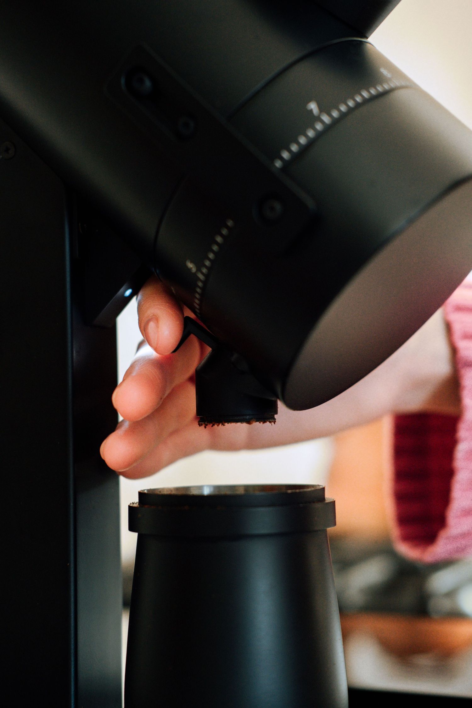 Hand adjusting settings on a professional black coffee grinder.
