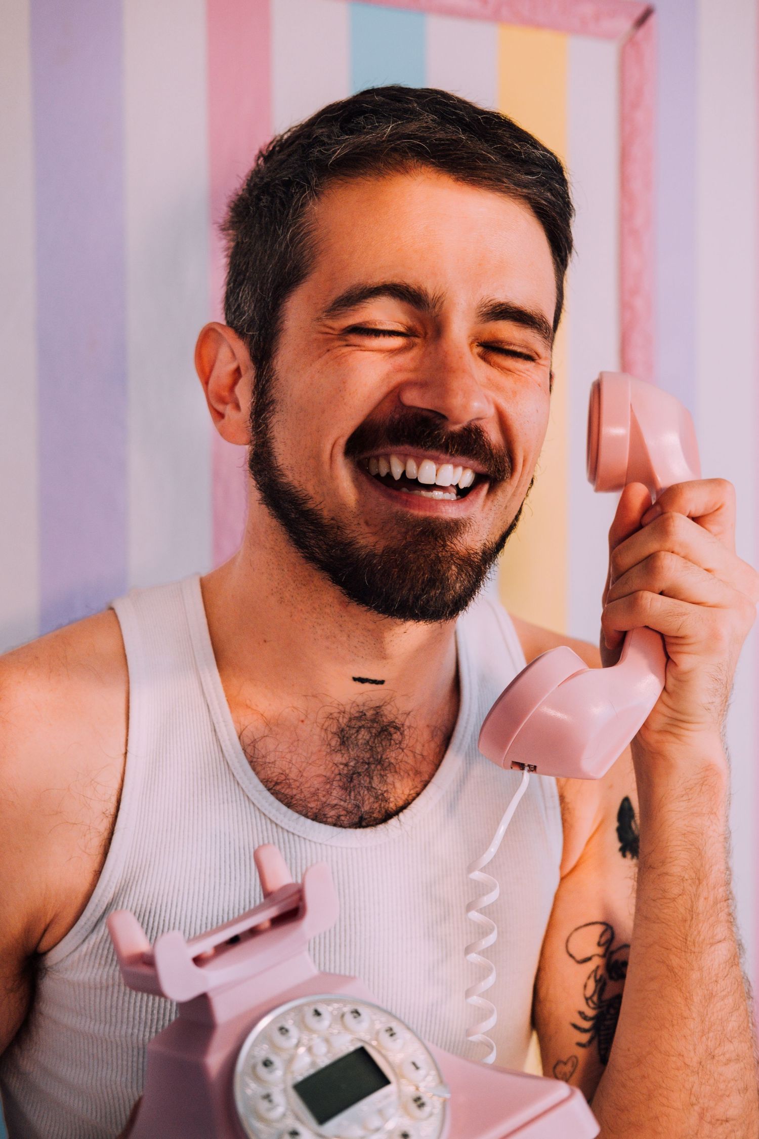 Queer consultant headshot, brightly colored & creative. They're holding a pink phone with a striped backdrop in a SF personal branding shoot