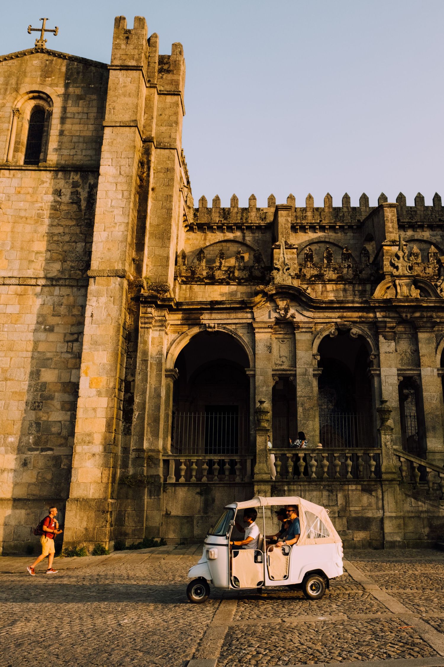 A small white tuk-tuk parked in front of a historic stone cathedral with ornate architecture.
