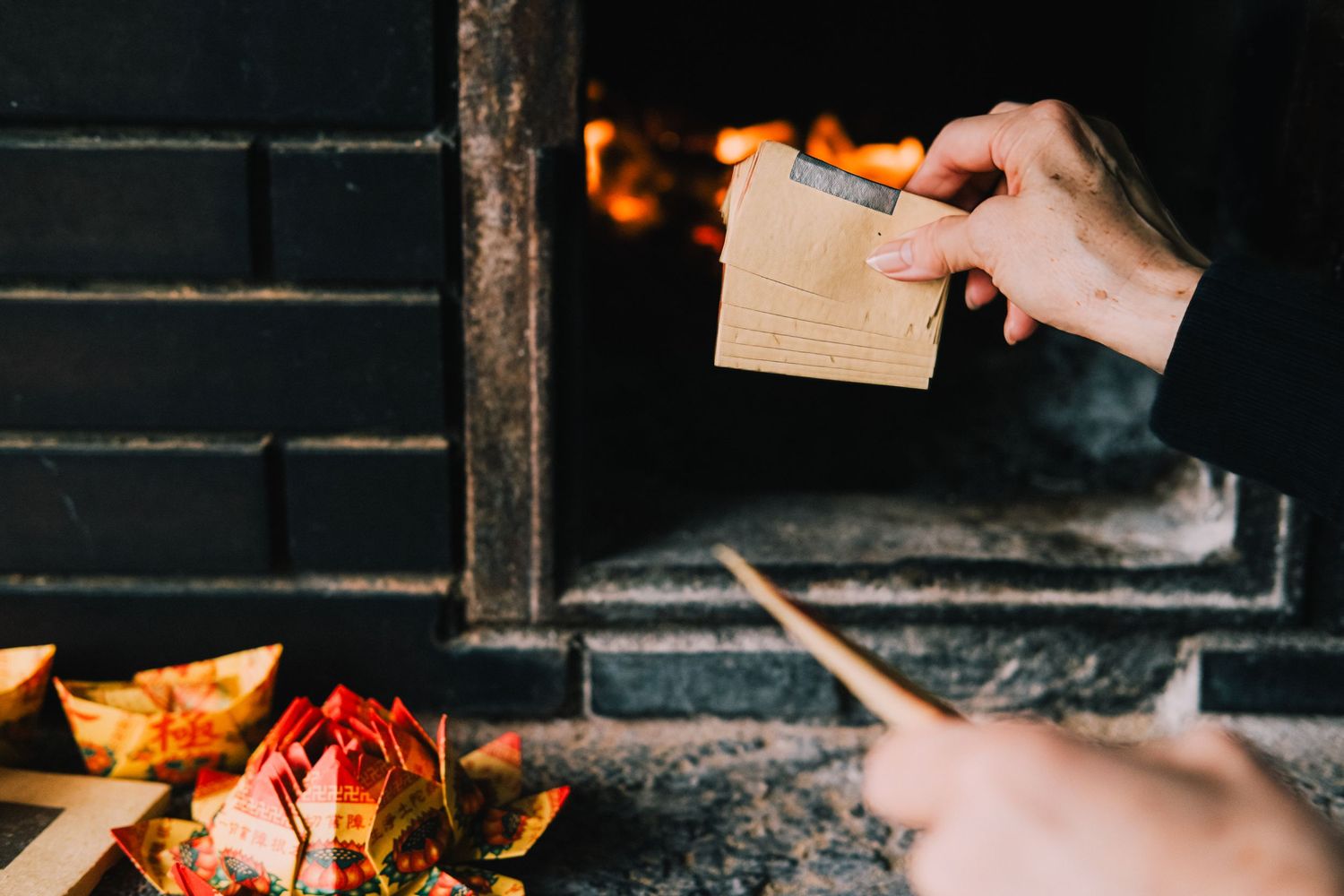 Hand placing a small wooden box into a rustic fireplace with autumn leaves scattered below.