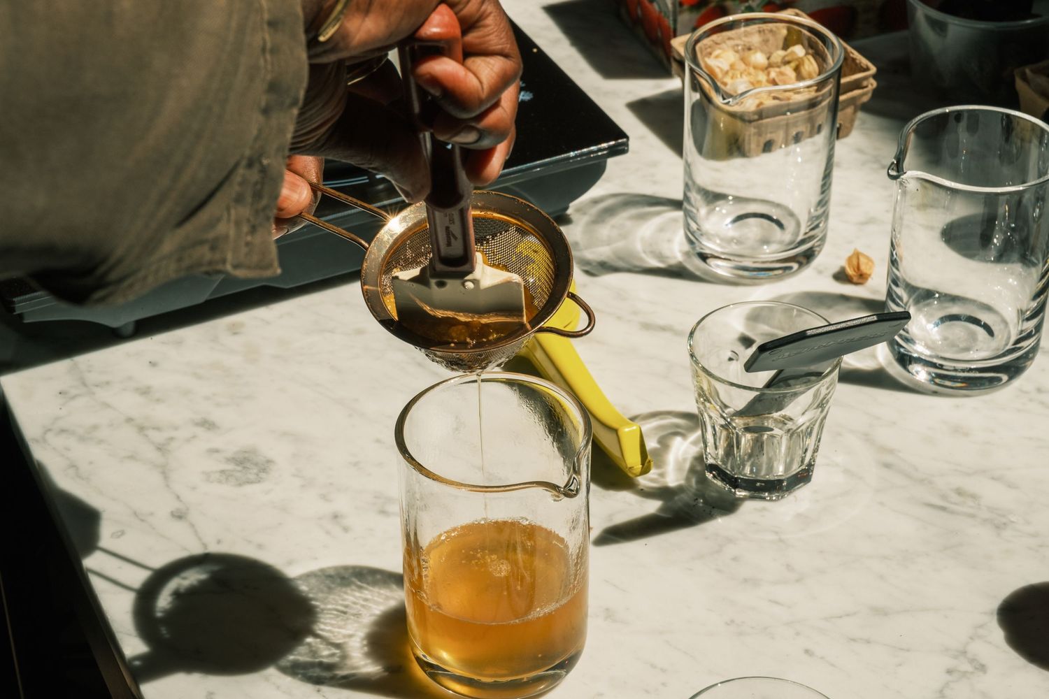 Tea being poured from a glass teapot into clear glasses on a marble countertop with ambient lighting.