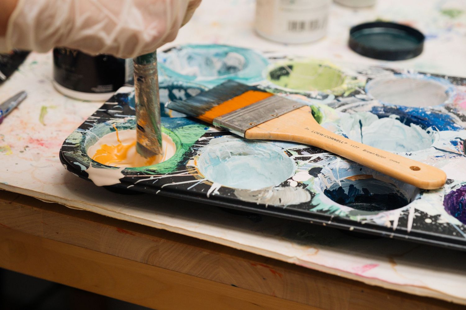 Artist's hand using watercolor paints and brushes to create colorful artwork on white paper.
