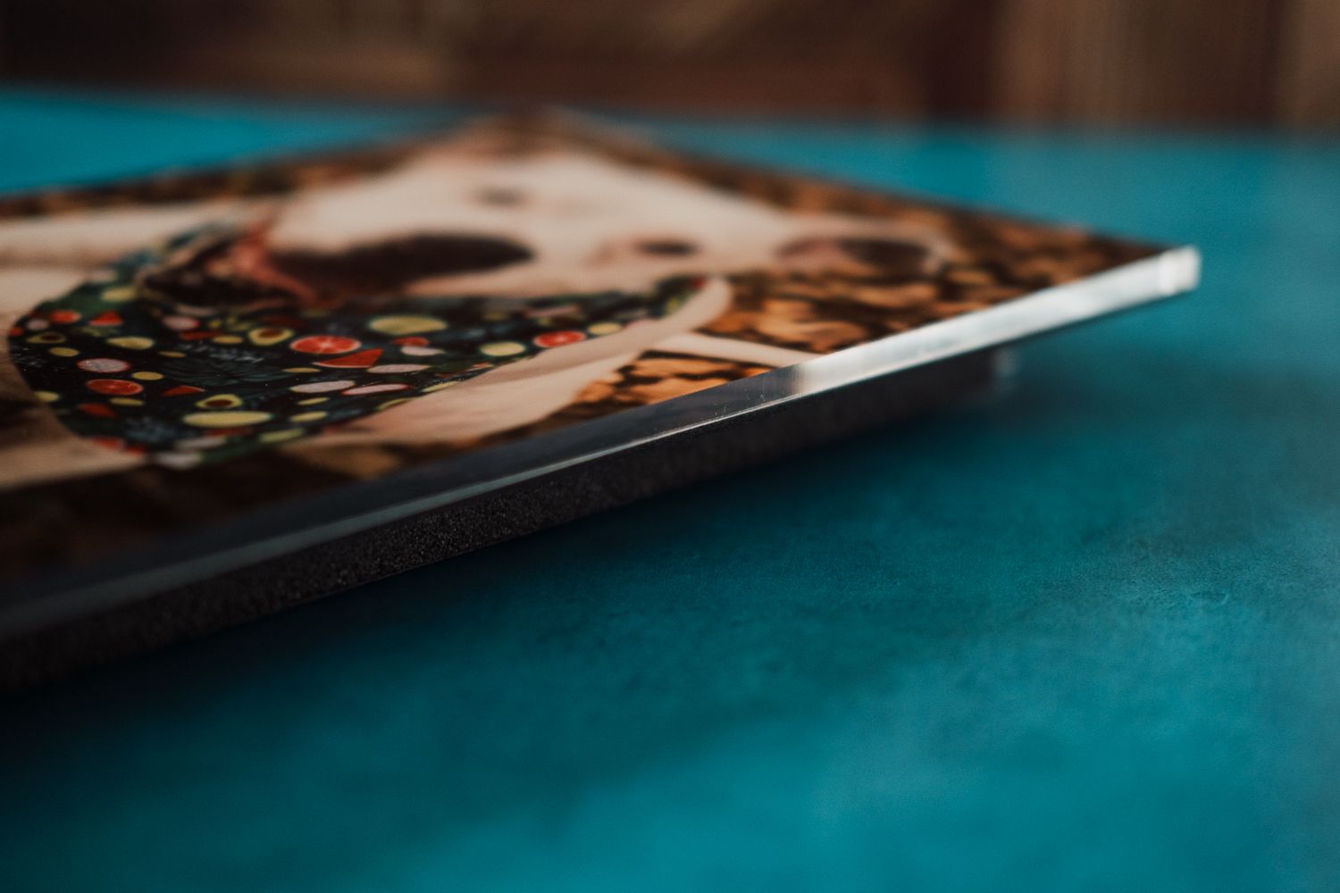 Close-up of a printed photo tile featuring a dog with a colorful floral collar, displayed on a teal surface.