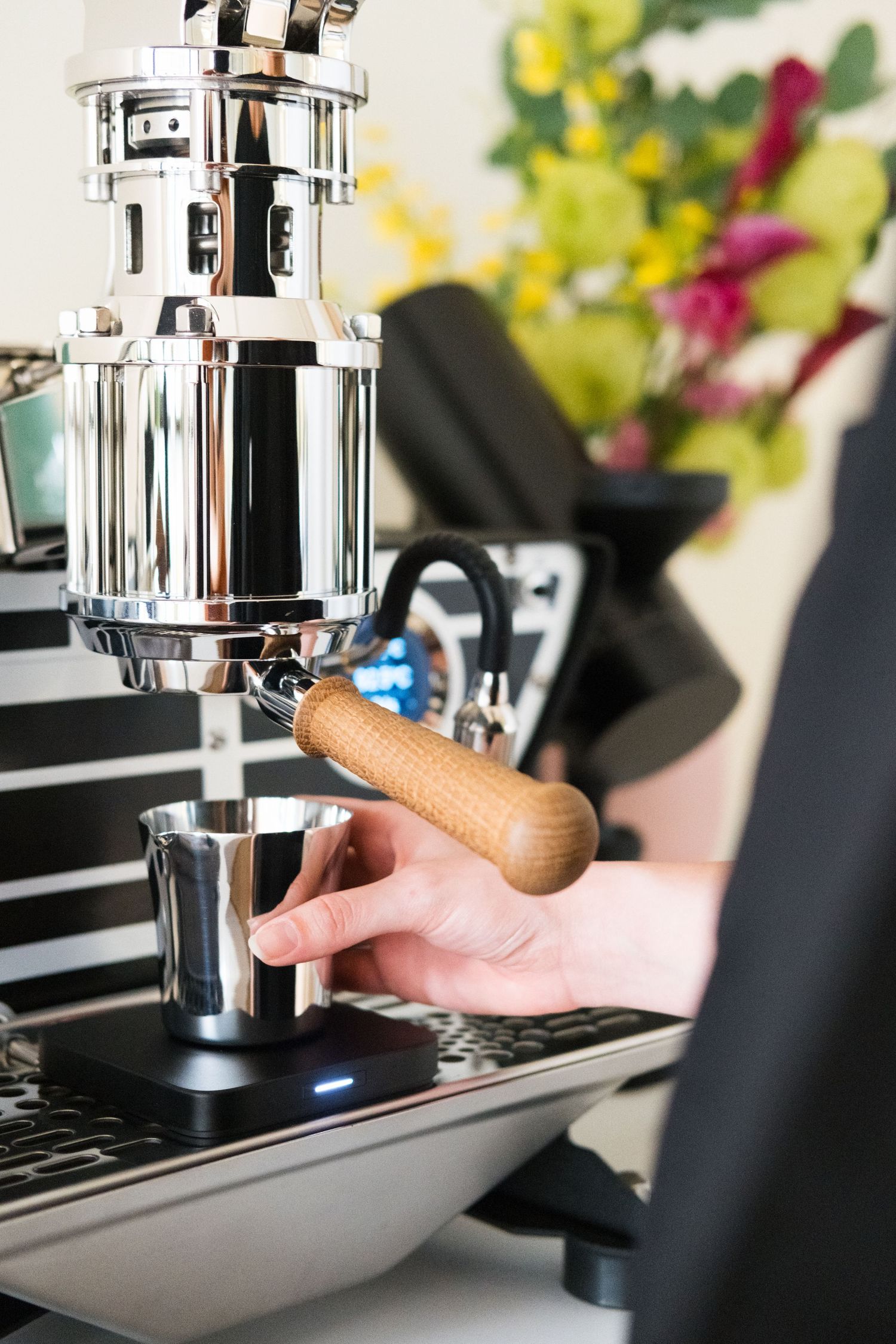 Coffee machine portafilter being tamped with wooden handle tamping tool on black espresso machine.