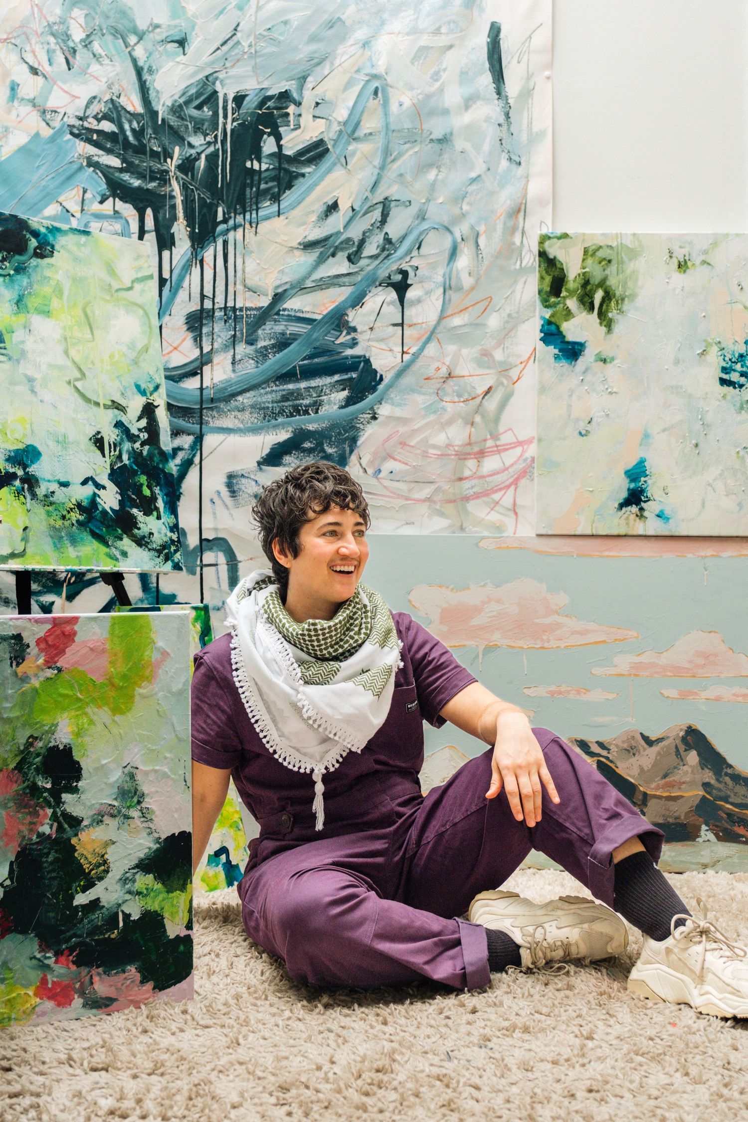 Abstract art gallery wall serves as backdrop for casual portrait session on white gravel floor.