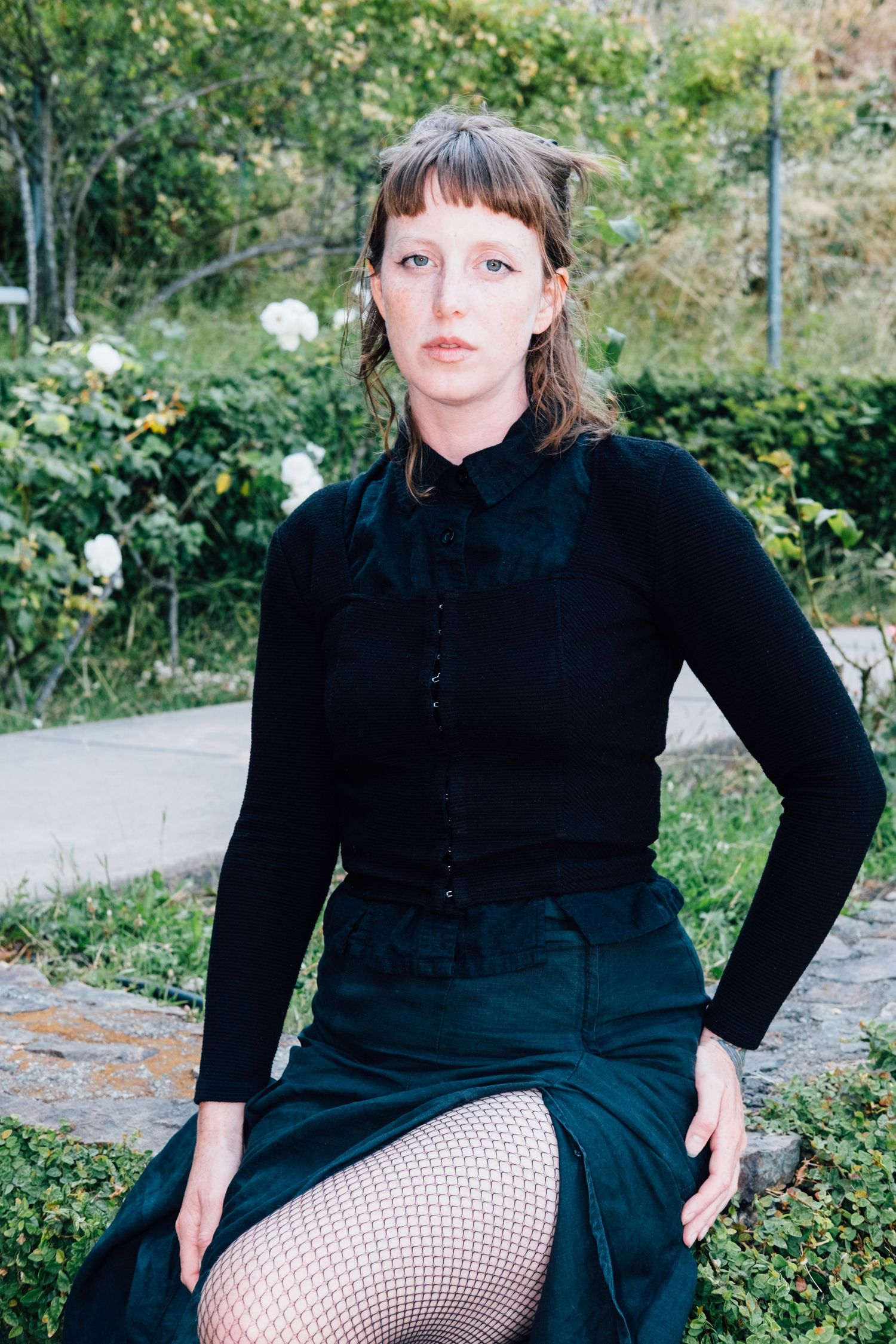 Fashion portrait in a garden setting with dark clothing and fishnet stockings.