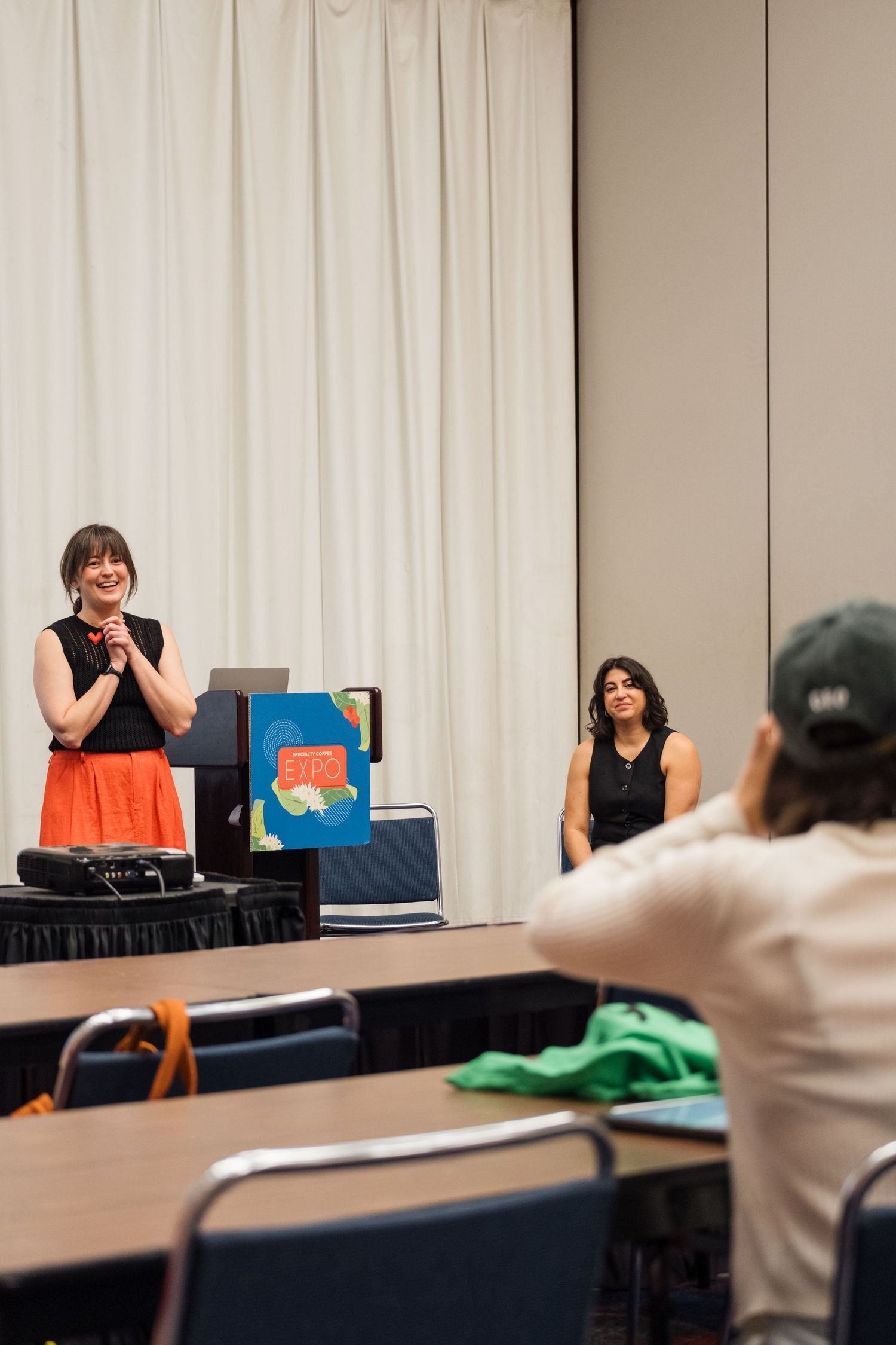 Presenter giving an enthusiastic presentation in a conference room setting with audience members.