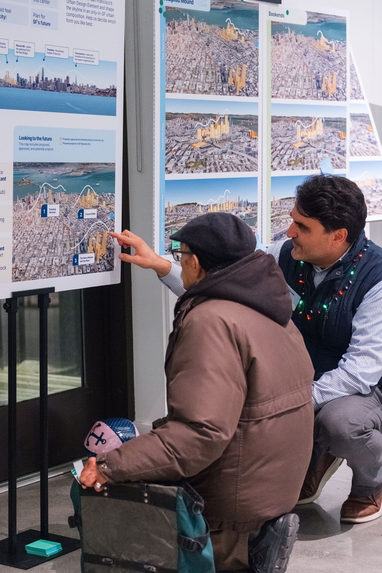 Two people examining urban landscape photographs displayed on wall during exhibition.