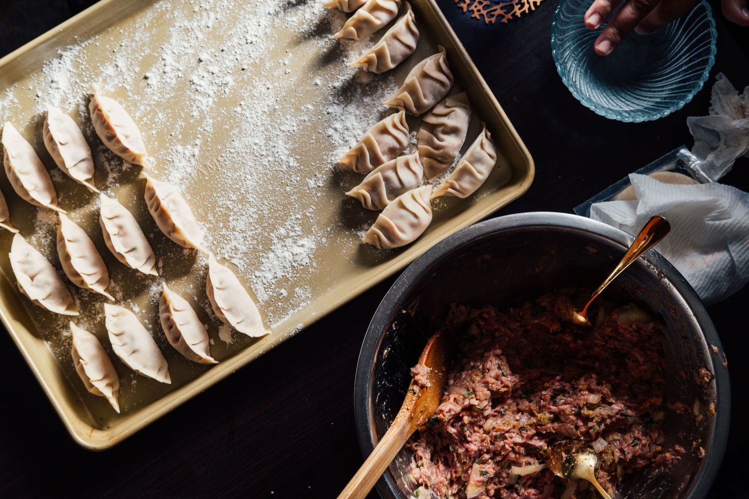 Homemade dumplings arranged on wooden boards next to a pan of dark sauce and chopsticks on a dark background.