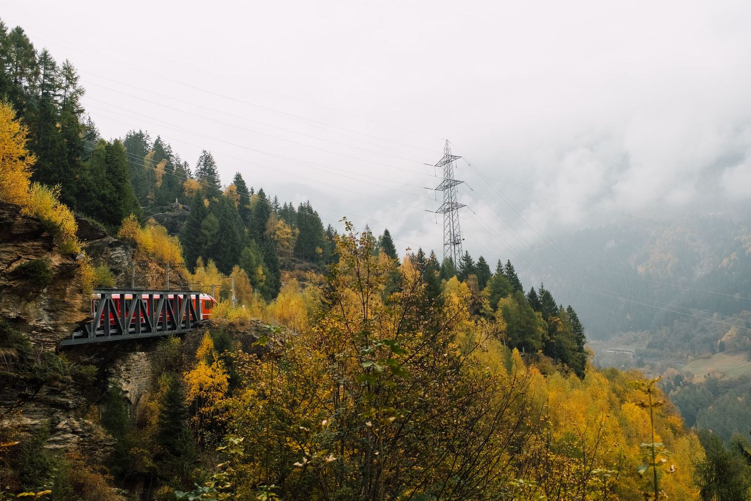 Misty mountain landscape with power lines stretching through autumn forest and yellow foliage in foggy conditions.