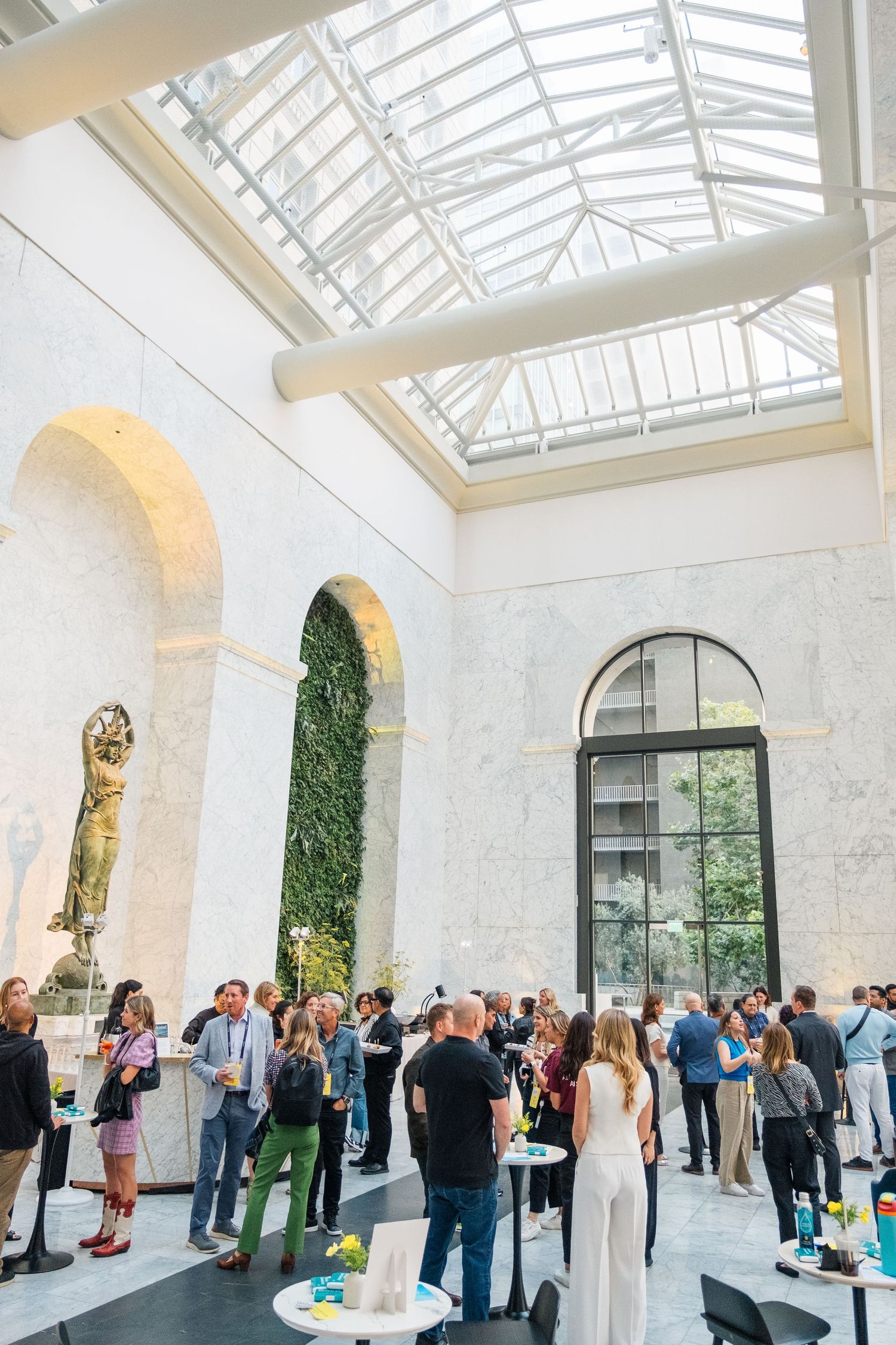 Guests mingle in an elegant event space with arched windows, skylights, and bright white walls during a social gathering.