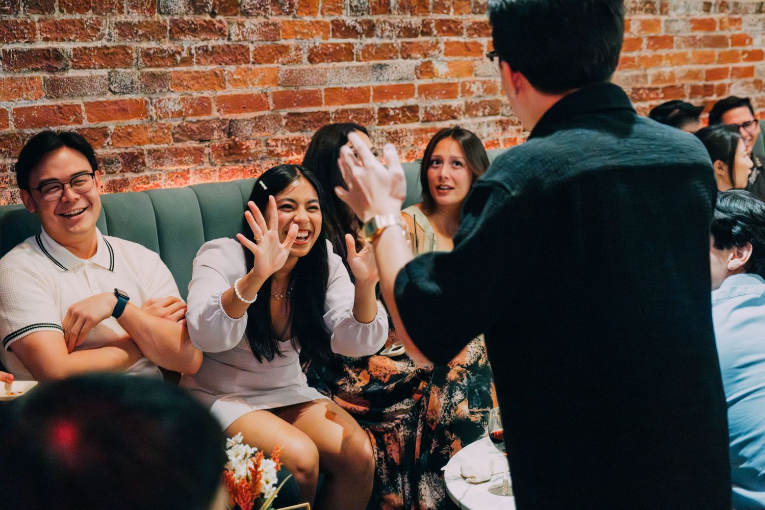 People engaged in animated discussion at an informal gathering with brick wall backdrop.