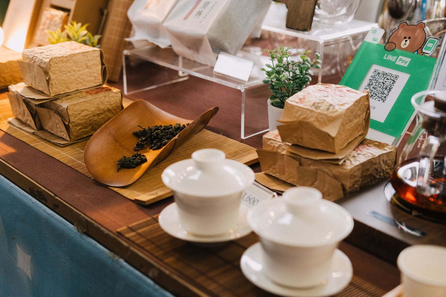 Wooden table display with multiple white ceramic teacups and brown paper packages arranged neatly in a cafe setting.