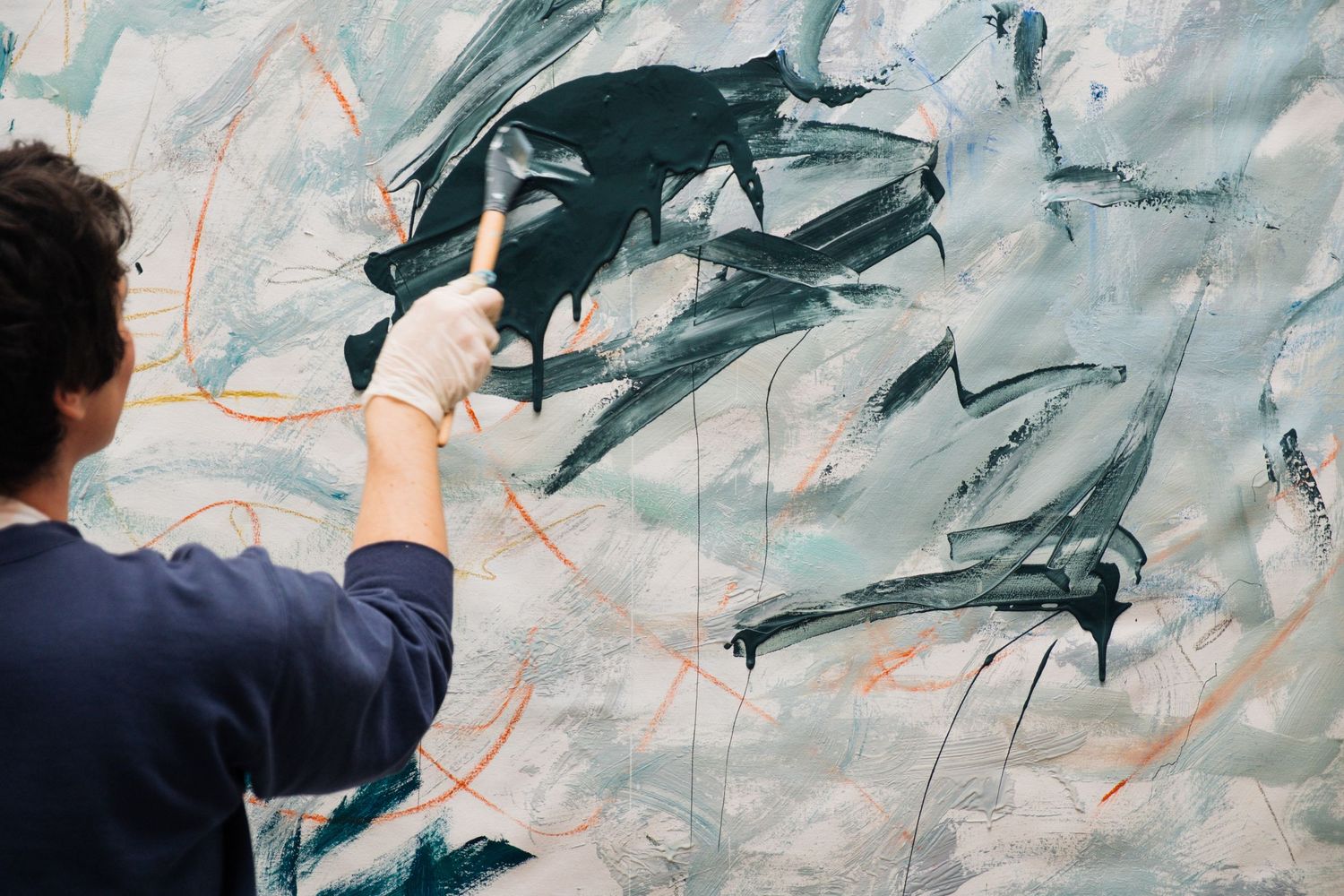 Artist works on large abstract mural painting with blue and gray tones on a white wall.