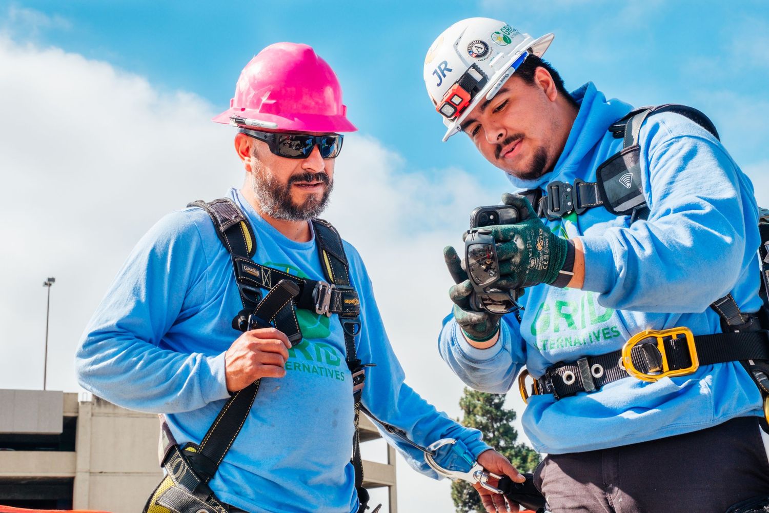 Two workers in safety gear operating camera equipment on outdoor job site.