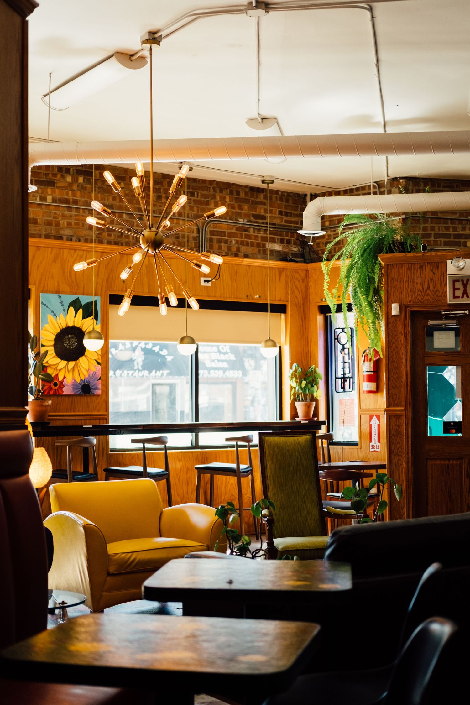 Cafe interior features warm wood paneling, yellow booths, and sunburst pendant lights creating a cozy retro ambiance.