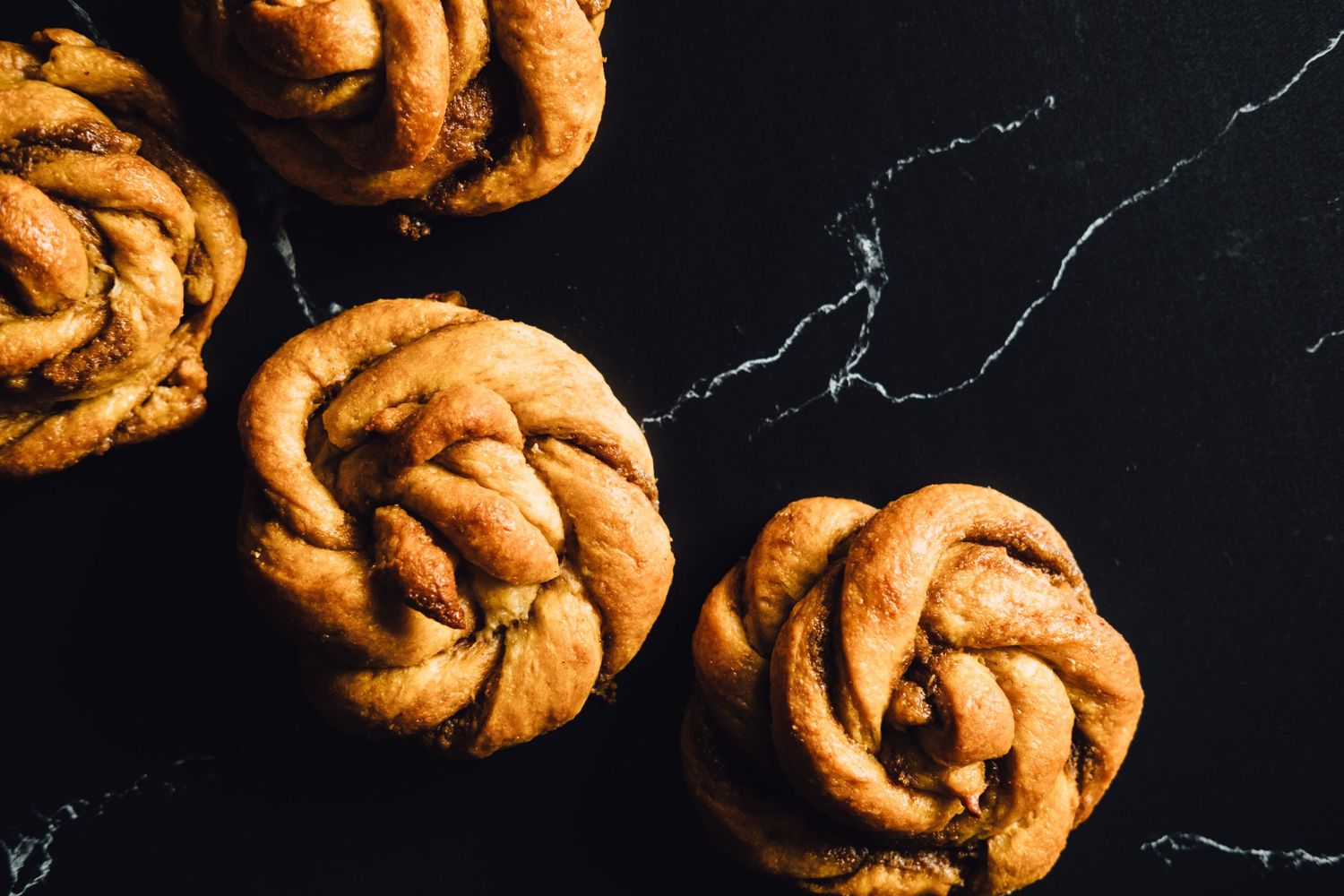 Artisanal twisted cinnamon buns arranged on a dark marble surface.