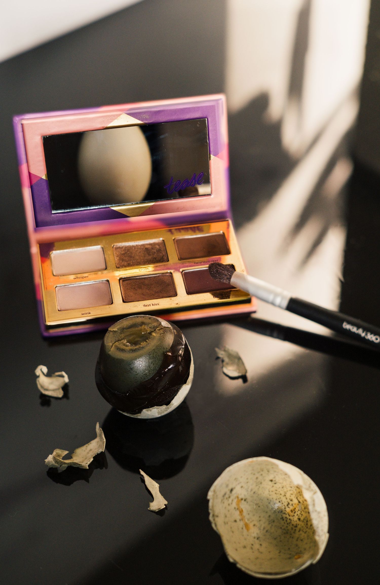 Close-up sequence of a black apple being cut open to reveal its interior against a dark background with makeup palette.