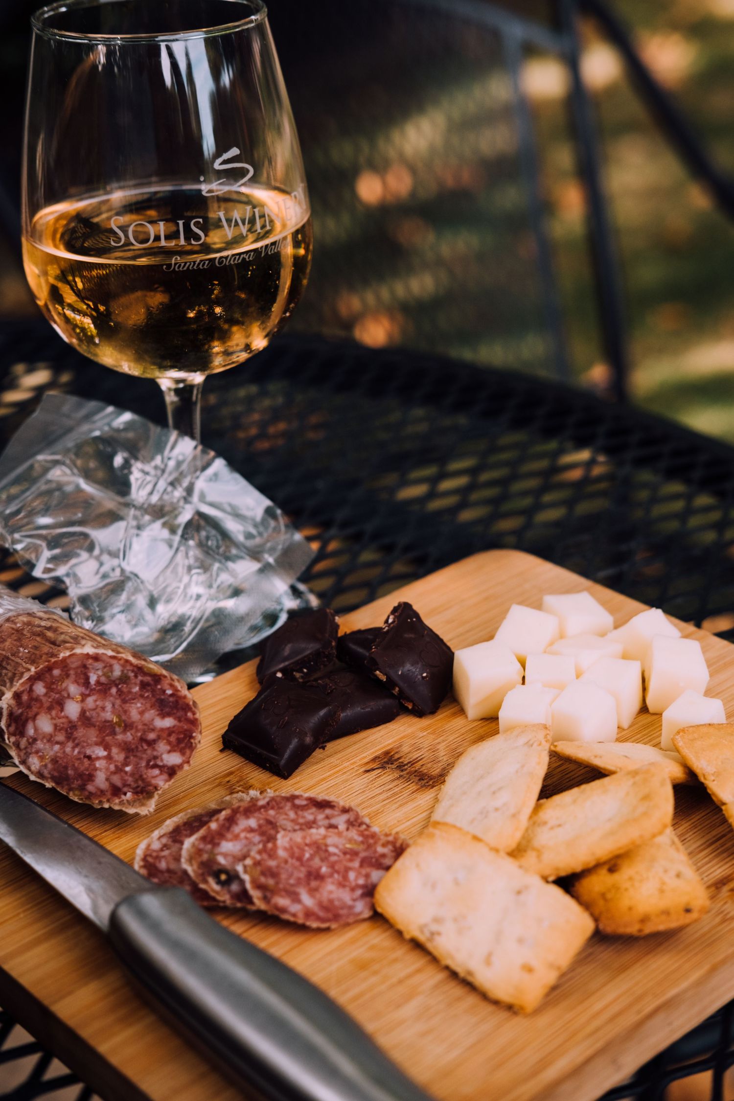 Wine glass and charcuterie board with meats and cheeses on outdoor patio table.