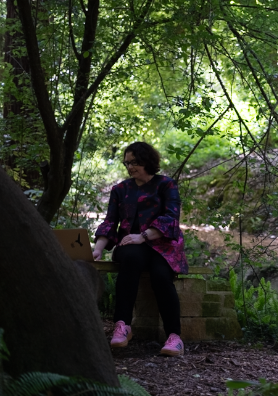 A person sits on stone steps surrounded by lush green foliage in a peaceful garden setting.
