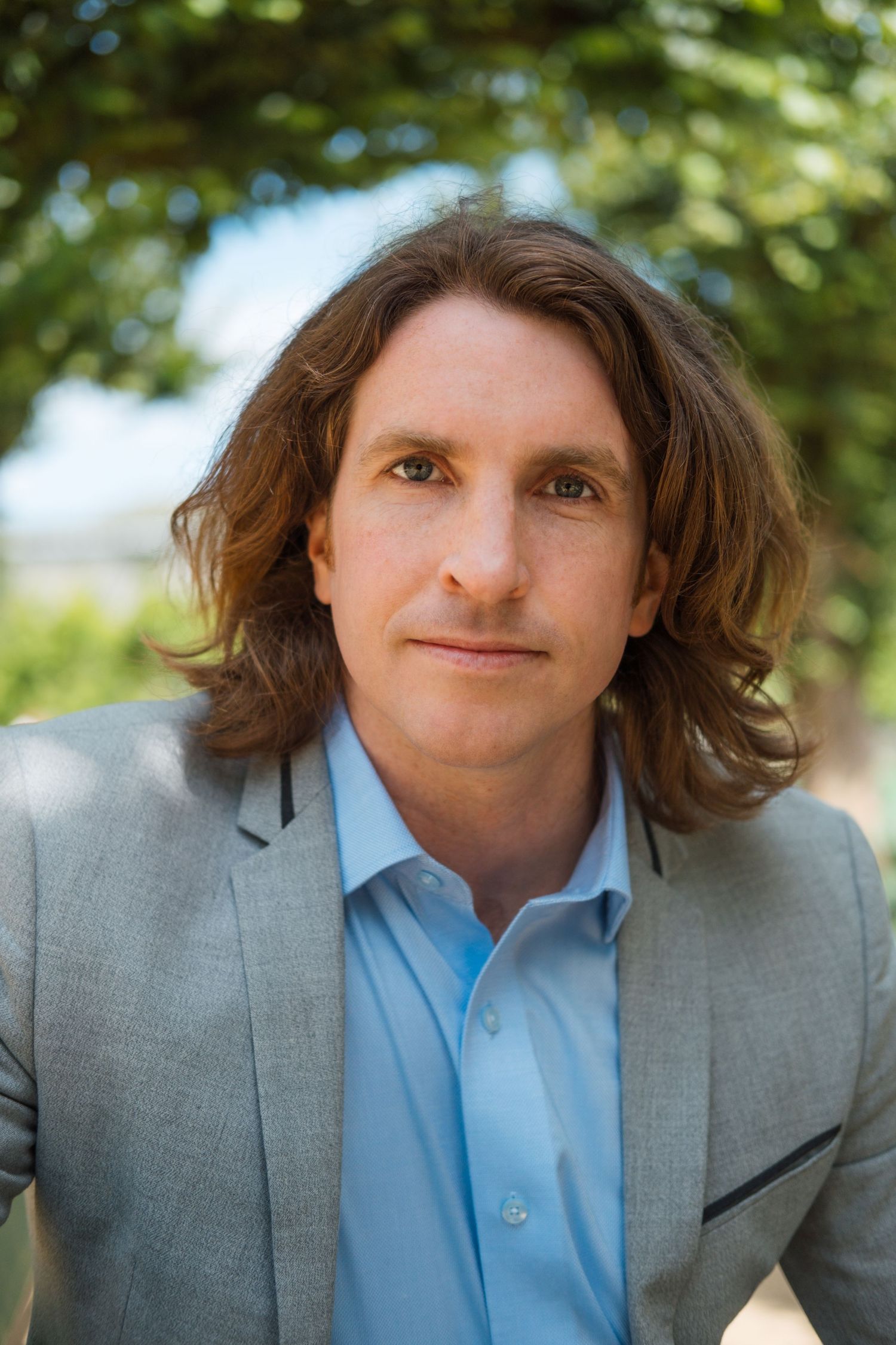 Serious business headshot, man with shoulder-length hair and suit looking straight into camera. SF Bay Area outdoor lifestyle headshot.