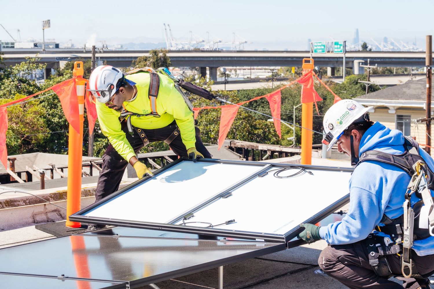 Workers in safety gear installing solar panels on an outdoor structure.