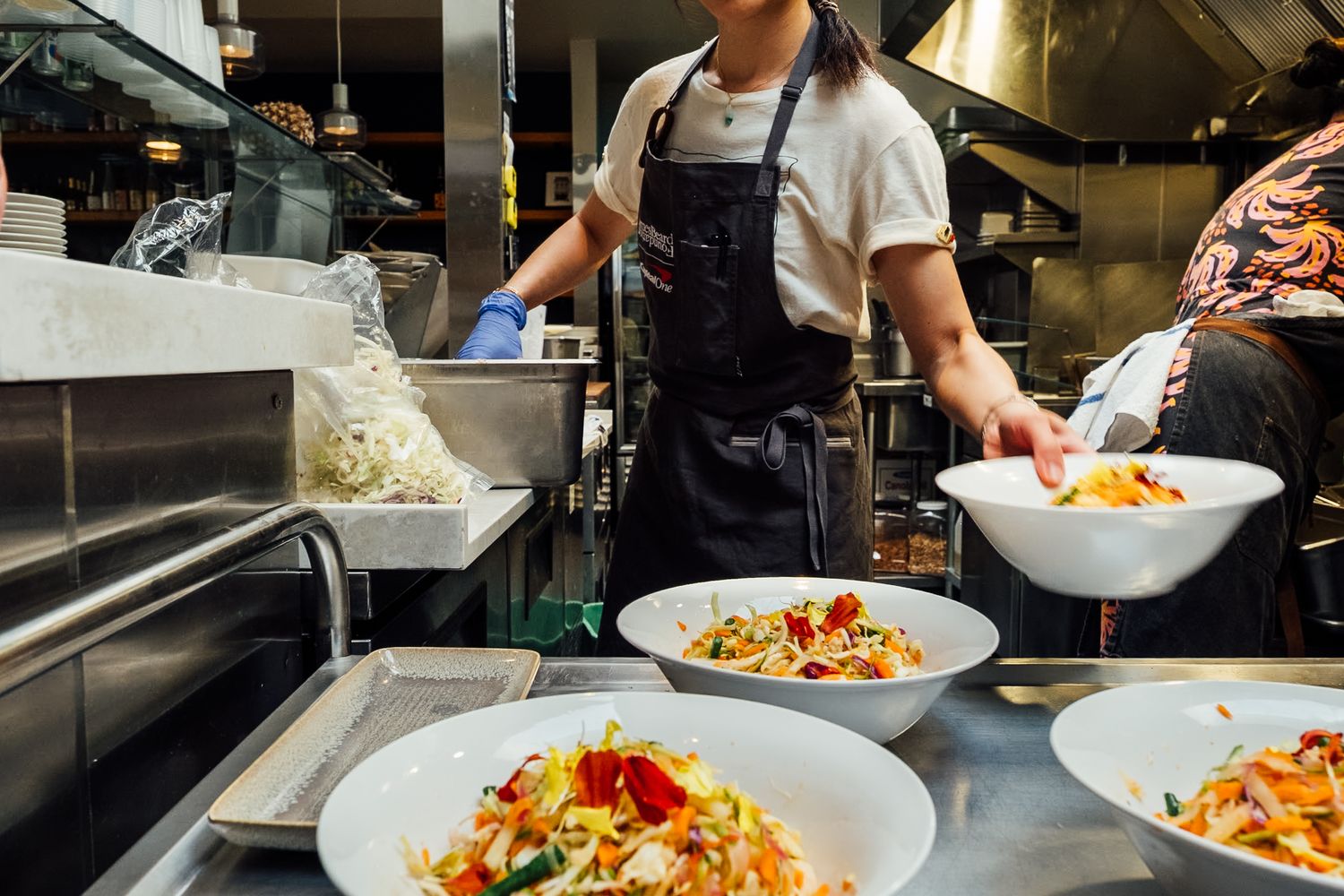 Chef plating colorful pasta dishes in busy restaurant kitchen.