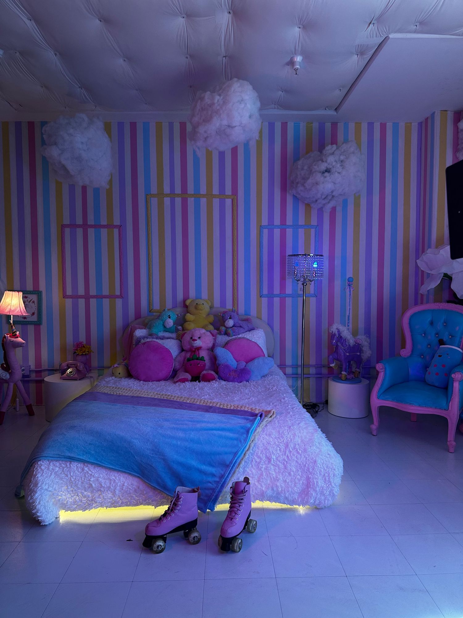 A whimsical bedroom with striped walls, fluffy cloud decorations, and colorful LED lighting creating a dreamy atmosphere.