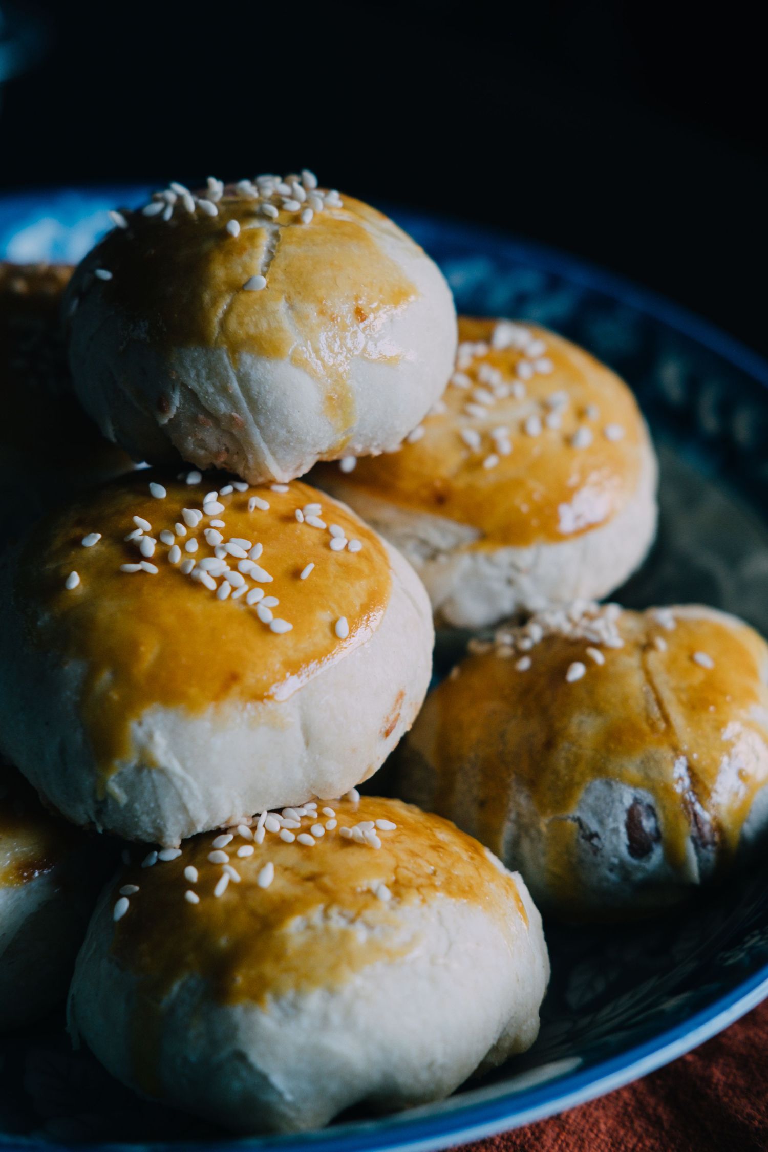 Fresh baked dinner rolls with sesame seeds arranged on a dark plate.