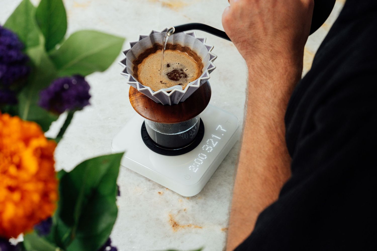 Coffee being brewed in a pour-over setup with colorful flowers in the background.