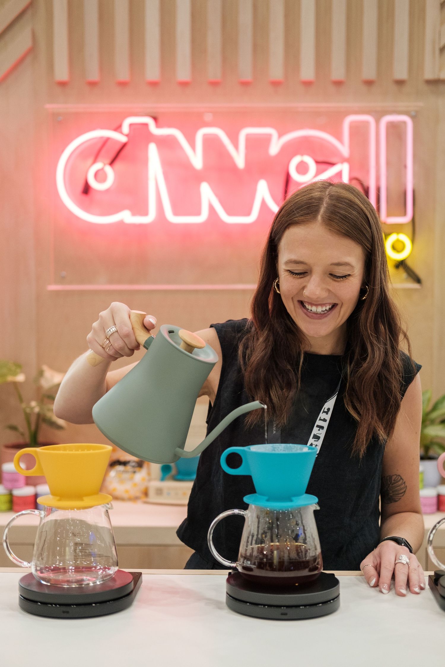 Barista demonstrating pour-over coffee brewing technique under neon signage.