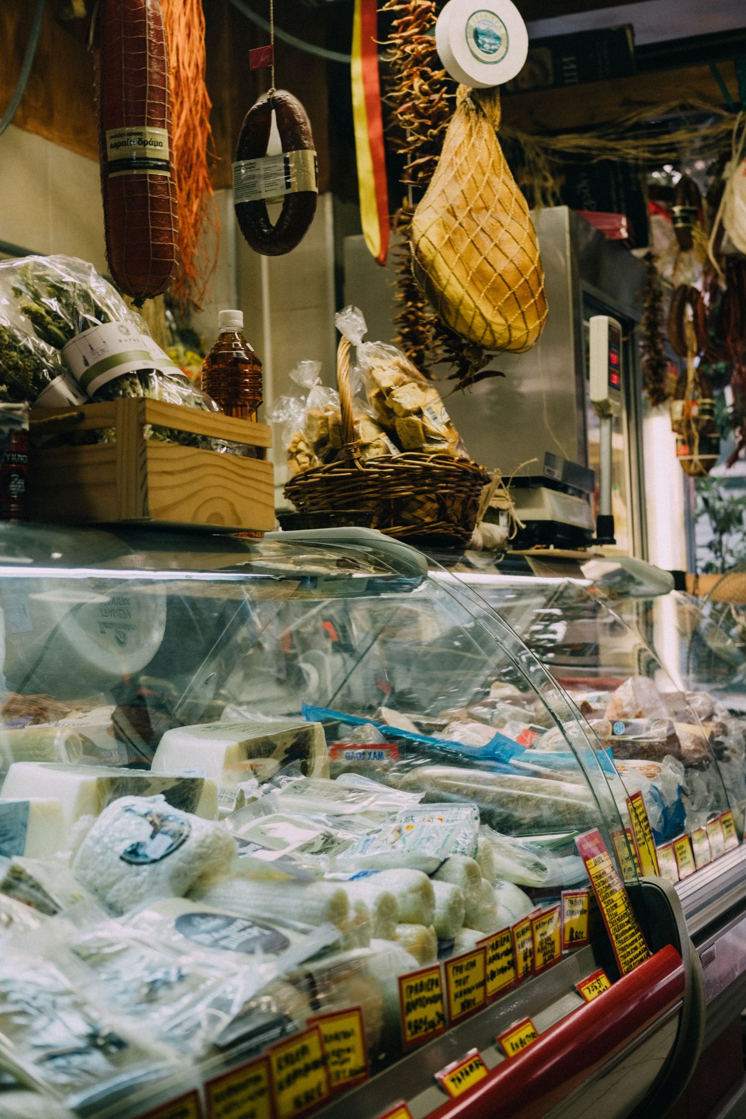 Delicatessen display case filled with meats and hanging cured products in a traditional market setting.