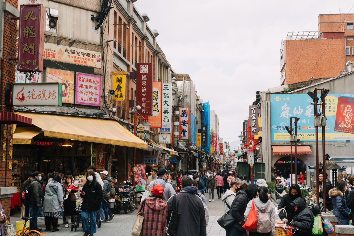 Busy street scene in Taiwan with colorful storefronts and crowds of shoppers walking along the sidewalk.