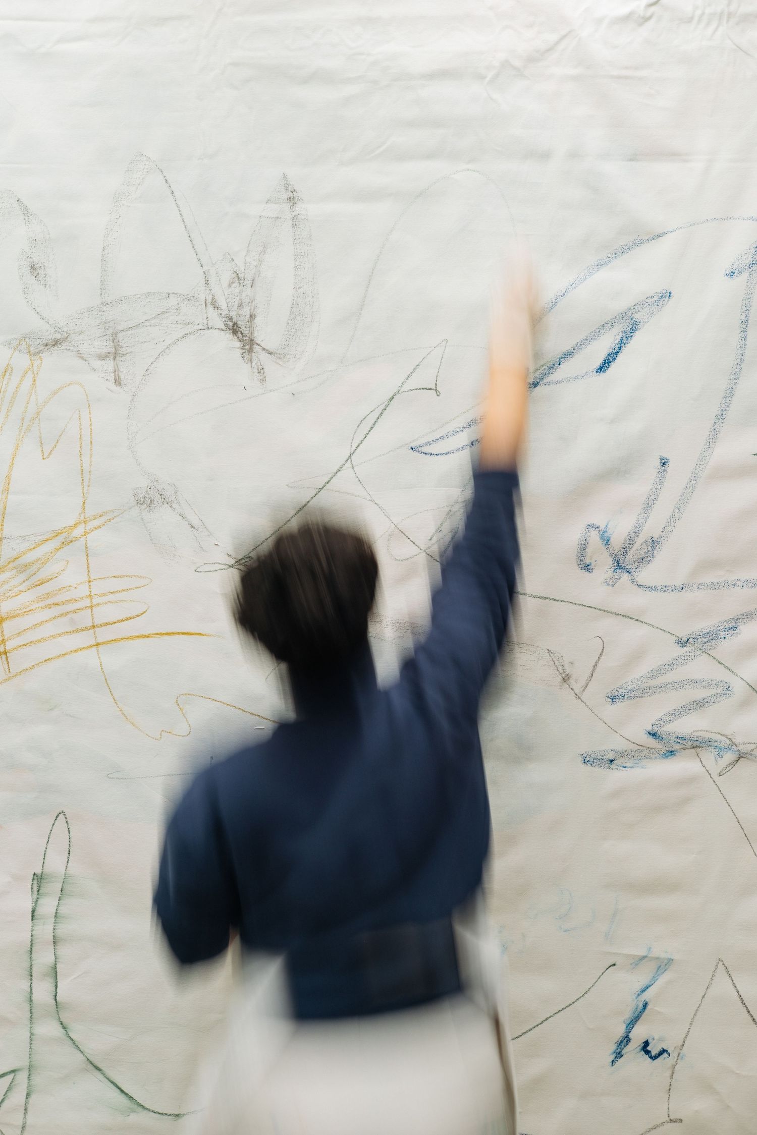 A sequence of motion blur images showing someone in a navy blue sweater drawing on a large white surface.