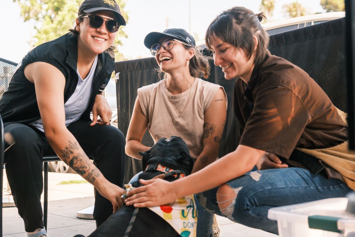 Group of friends petting black dog while sitting outdoors together.