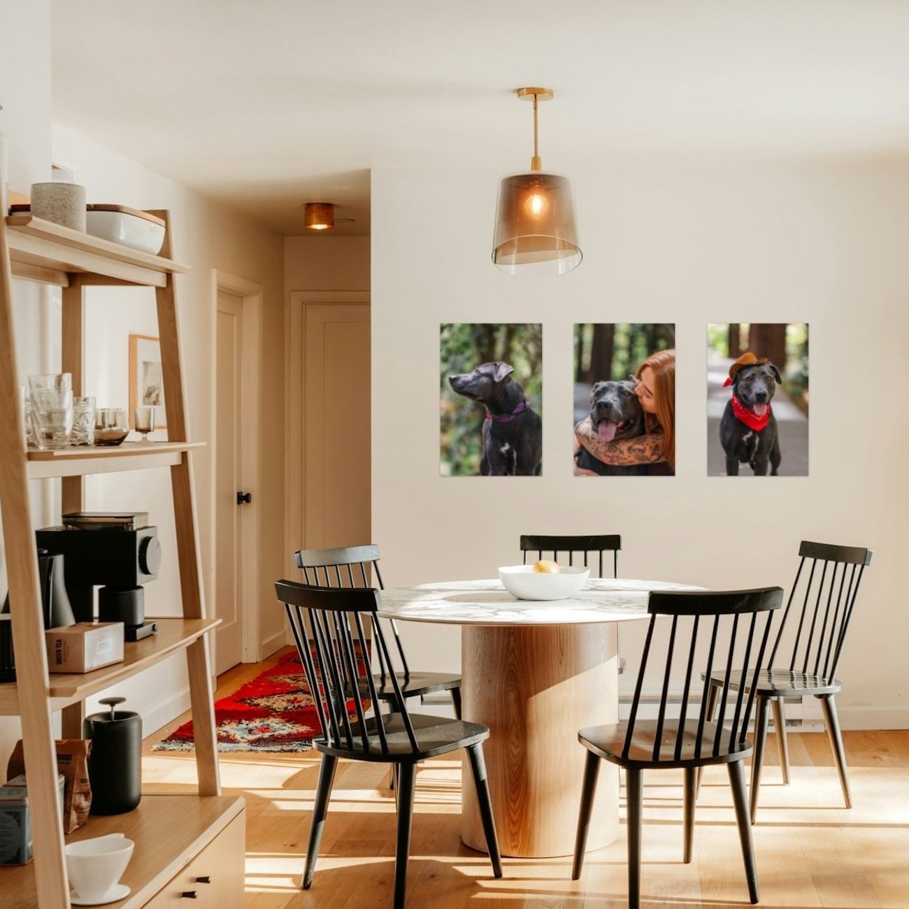 Bright dining room with round wooden table, black chairs, wood shelving, and two black dog portrait canvas prints on the wall.