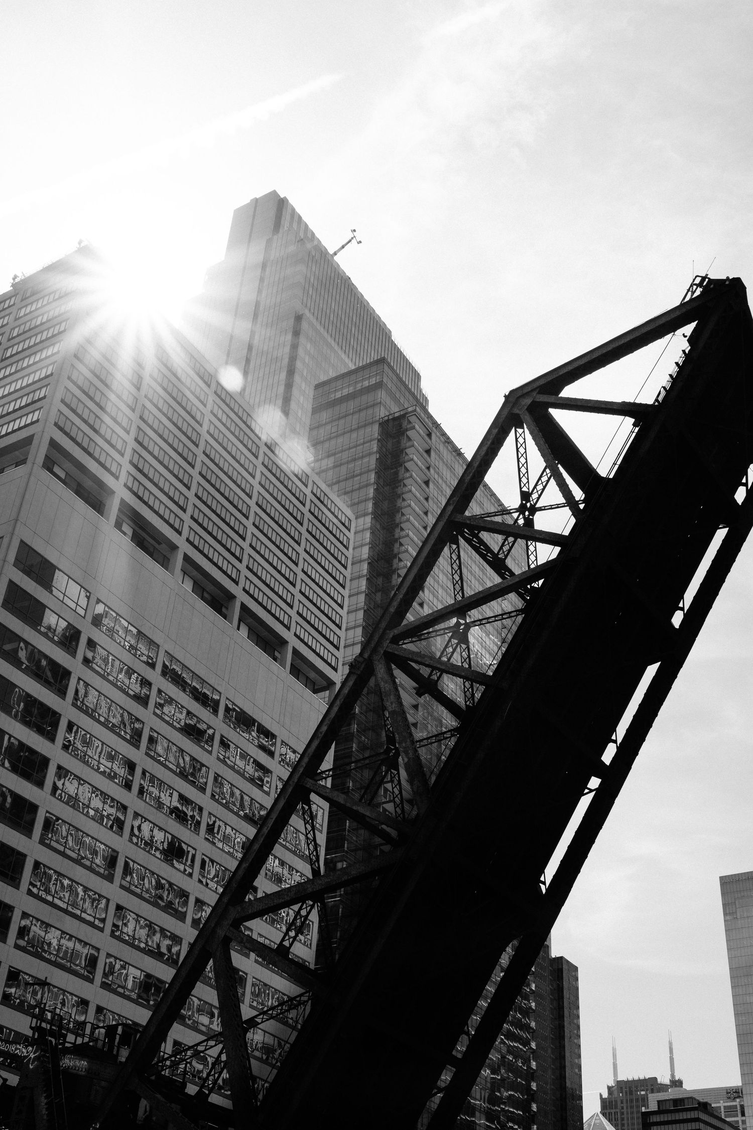 Modern skyscraper and industrial bridge photographed against bright sunlight in black and white.