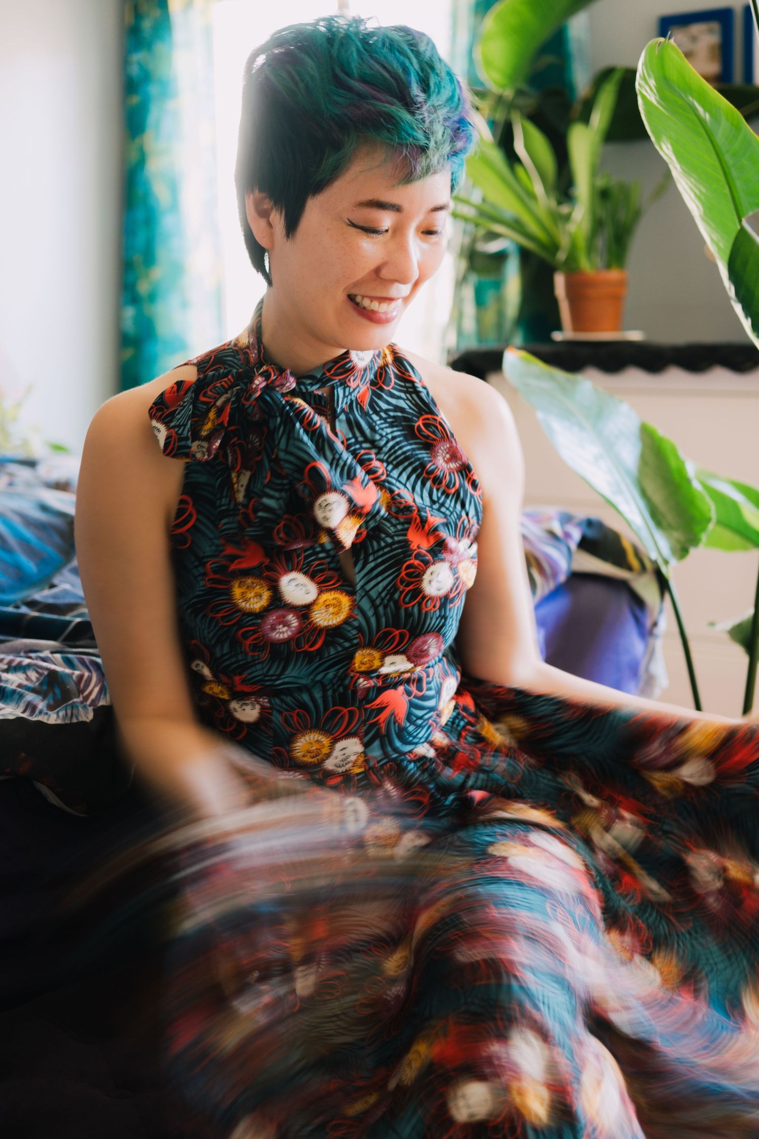 A floral print dress flows with movement in a sunlit room with houseplants.