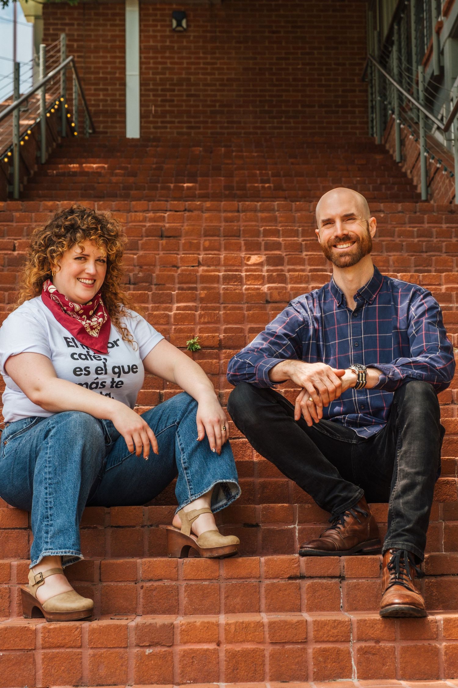 Two people sit casually on red brick steps outside a building entrance.
