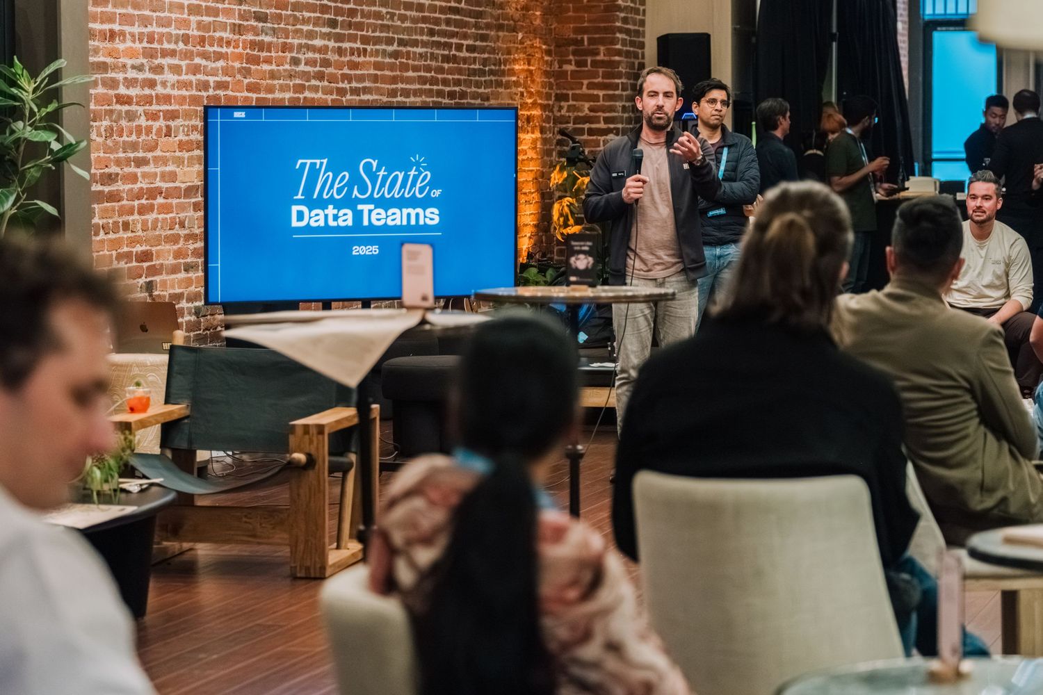 A presentation or meeting taking place in an office space with exposed brick walls and a large blue screen display.