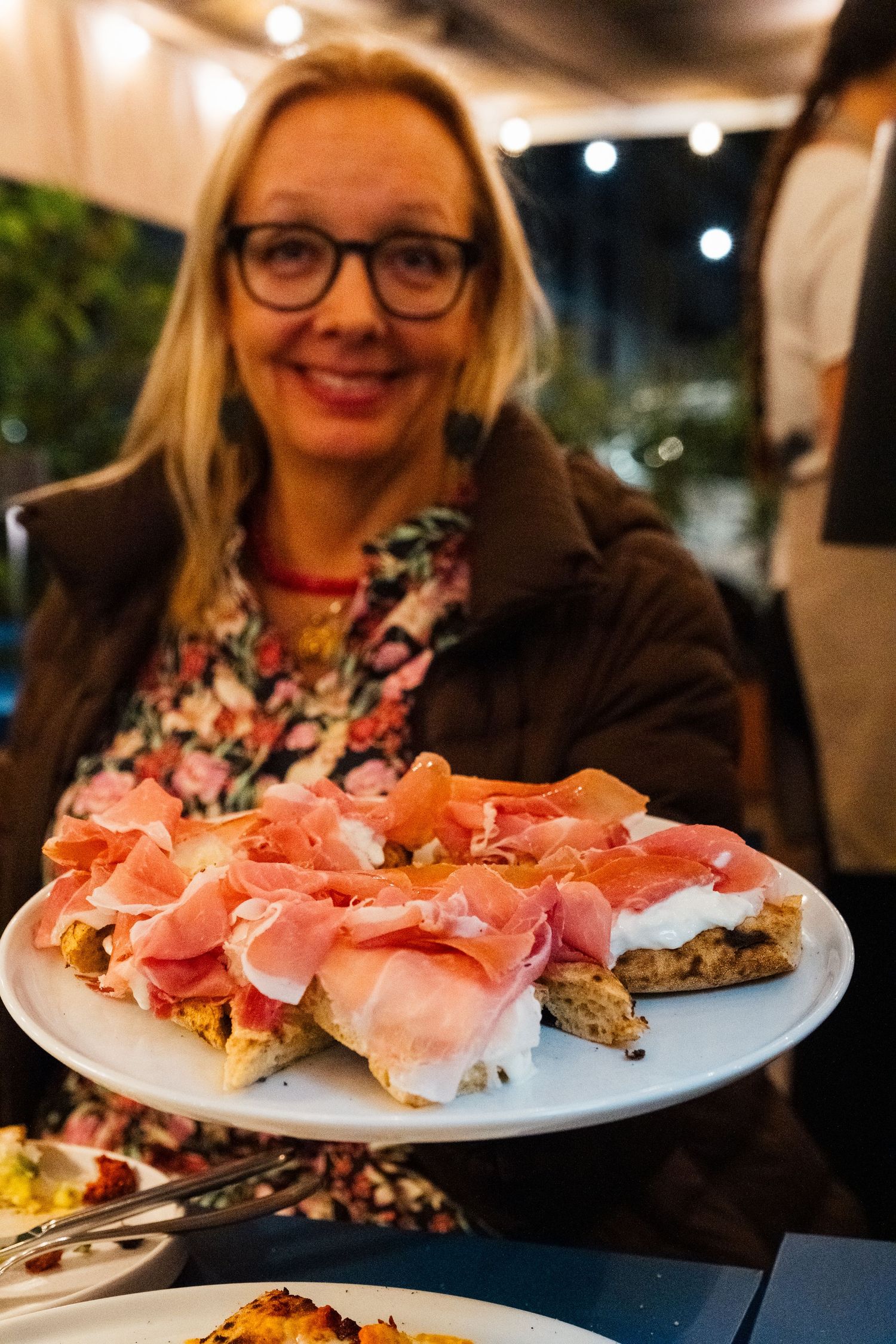 Plates of prosciutto ham appetizers served on a restaurant table with diners in the background.