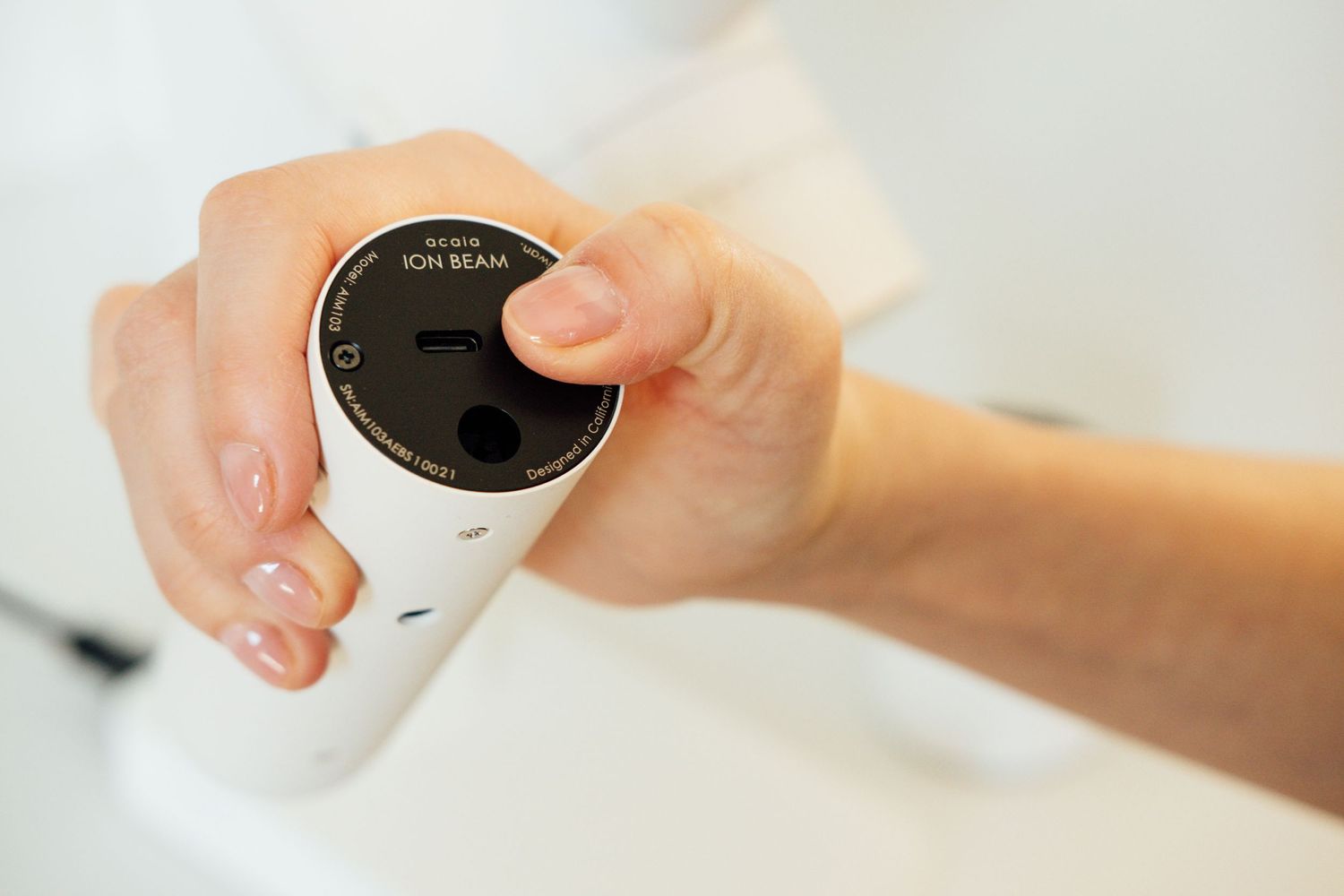 Hand holding a white cylindrical container with a black lid.