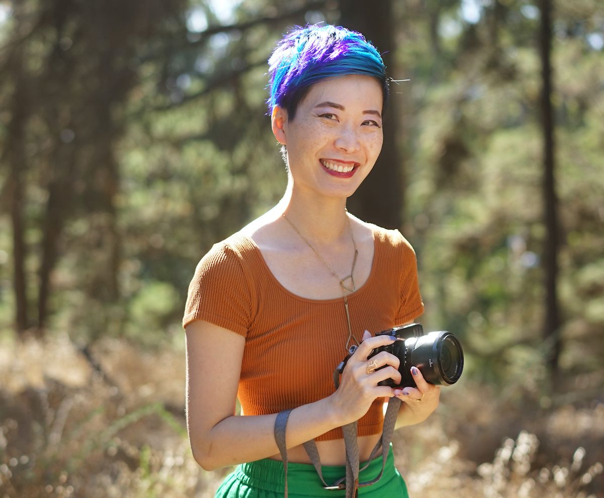 Outdoor photographer with colorful hat holding camera in forest setting.