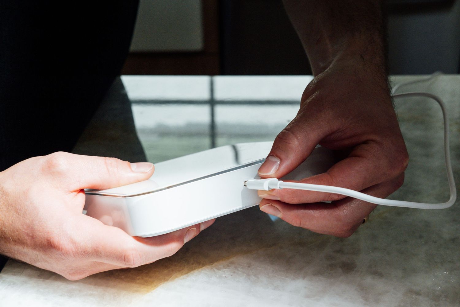 Hands holding and examining a white electronic device on a counter surface.