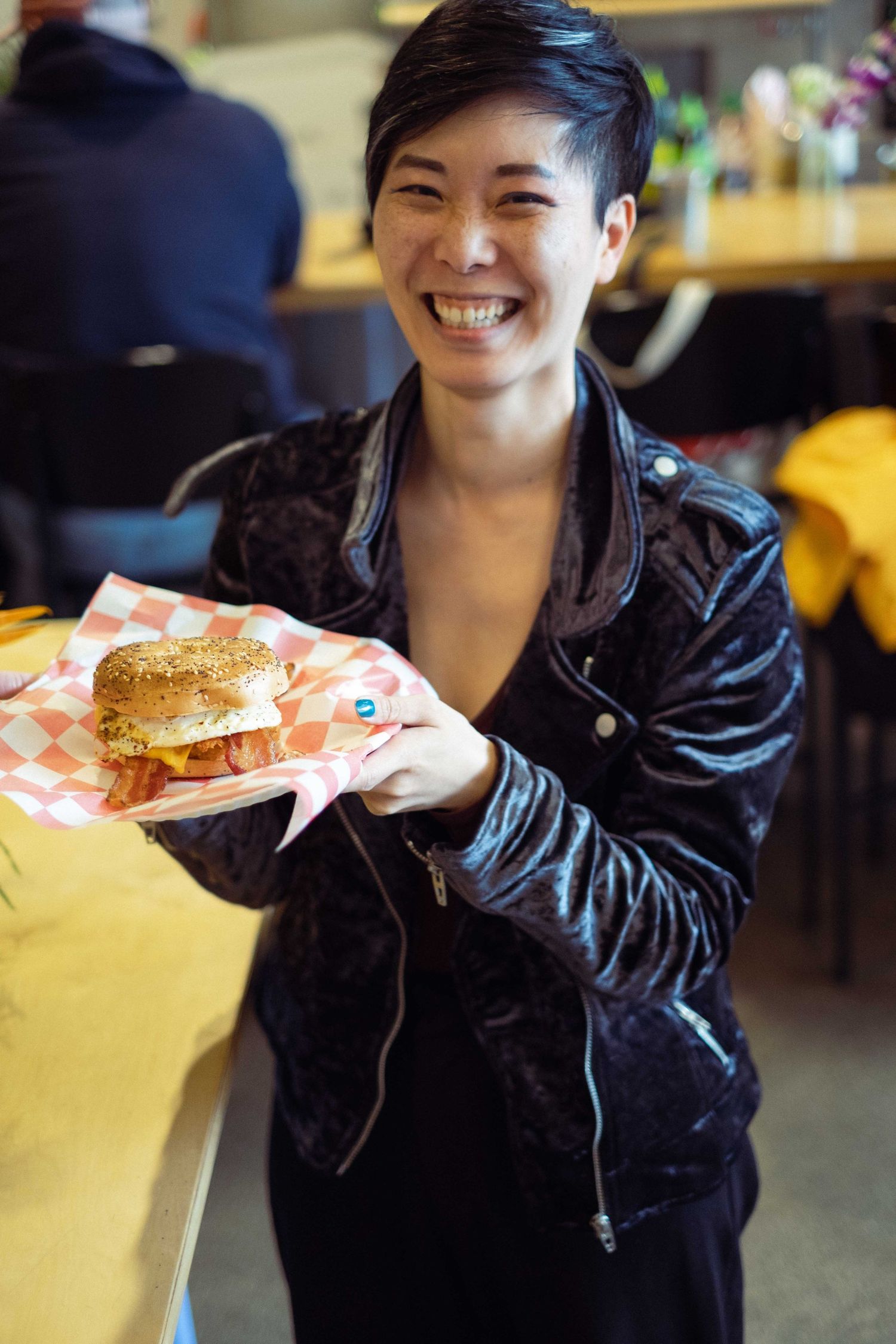 Casual diner scene with person holding a fresh sandwich while wearing a black leather jacket.
