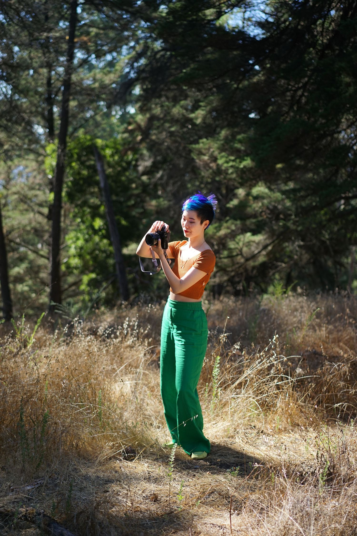 Photographer wearing blue cap and vibrant outfit captures images in golden forest setting.